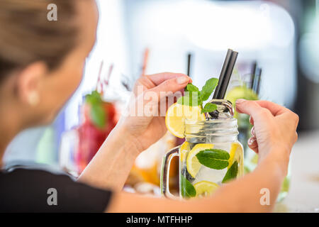 Jolie jeune femme avec un beau sourire tout en travaillant dans un bar la préparation de limonades. Banque D'Images