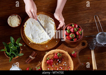 Close up of girl's hands ajouter la crème fouettée certains sur le haut de délicieux gâteau aux fraises, selective focus. Pâtisserie savoureuse est sur la table en bois Banque D'Images