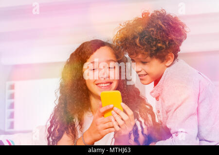 Piscine shot of teenage boy and girl using yellow téléphone mobile, SMS dans les réseaux sociaux Banque D'Images