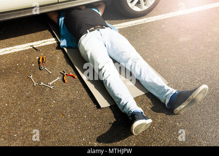 L'homme couché sous auto pont à faire un travail de réparation, en utilisant des clés et pinces à la rue Banque D'Images