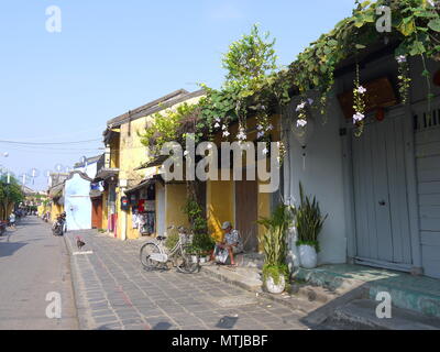 HOI AN, VIETNAM - 17ème Mars 2018 : Un homme assis sur un pas en avant d'un atelier fermé journal lecture début de matinée ensoleillée à Hoi An Banque D'Images