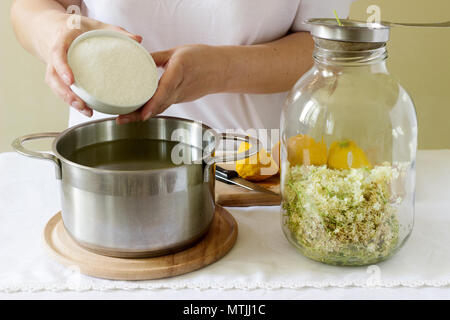 Des fleurs, de l'eau, de citron et de sucre, les ingrédients et une femme en train de préparer un sirop de sureau. Style rustique. Banque D'Images