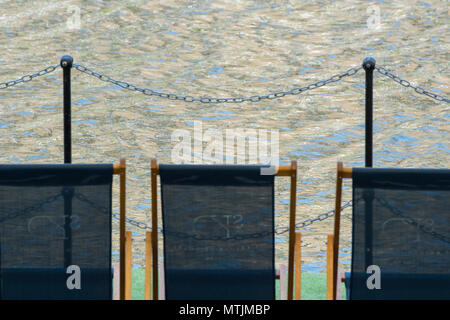 Trois chaises vides au bord de l'eau sous le soleil d'été dans le temps chaud sur certains meubles ou une jetée à côté de l'eau. au soleil au bord de mer. Banque D'Images