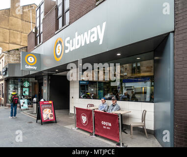 Deux jeunes hommes dans le coin salon extérieur Costa en face de Hillhead Subway Station dans Byres Road, Glasgow ; un autre homme regarde dans l'intermédiaire du Starbuck Banque D'Images