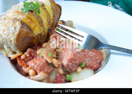 Une partie de Corned Beef hash servi avec un fromage surmontée de pommes de terre Hasselback Banque D'Images