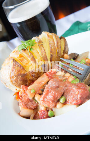 Une partie de Corned Beef hash servi avec un fromage surmontée de pommes de terre Hasselback Banque D'Images