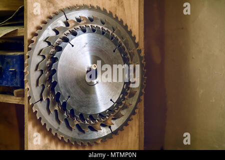 De nombreuses lames de scie circulaire en métal de tailles différentes sur un fond de bois en atelier Banque D'Images