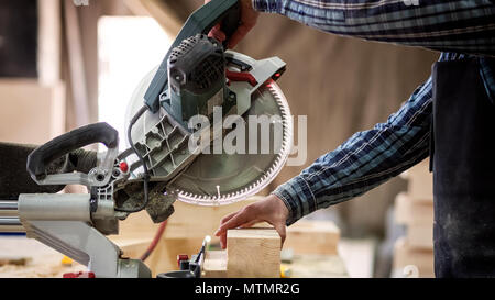 Carpenter en vêtements de travail faisant la menuiserie dans la menuiserie. petit buiness propriétaire coupe sur la planche en bois avec une scie circulaire en atelier Banque D'Images