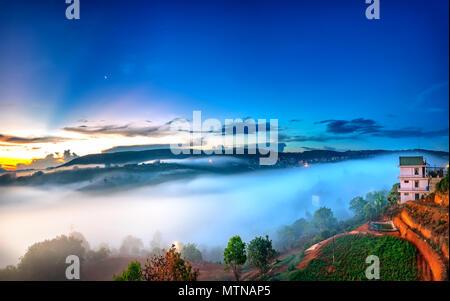 L'aube sur plateau en matinée avec ciel coloré, tout en passant de soleil éclaire l'horizon à petit village recouvert de paysage enveloppé de brouillard Banque D'Images