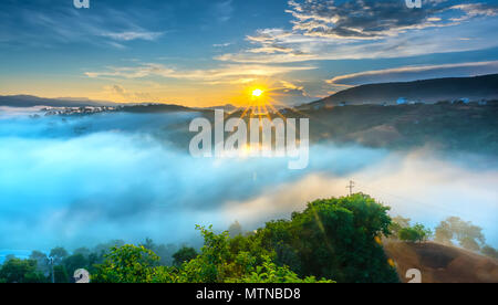 L'aube sur plateau en matinée avec ciel coloré, tout en passant de soleil éclaire l'horizon à petit village recouvert de paysage enveloppé de brouillard Banque D'Images