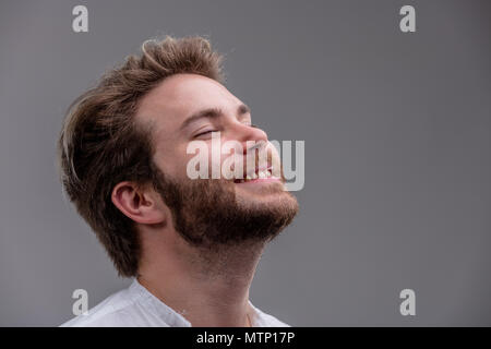 Jeune homme barbu détendue de bonheur avec sa tête inclinée en arrière, les yeux clos et un sourire rayonnant isolé sur gray with copy space Banque D'Images