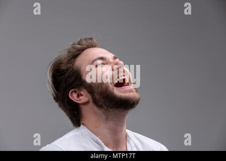 Fun jeune homme avec un sens de l'humour d'un rire avec sa tête rejetée en arrière et la bouche ouverte isolé sur gray Banque D'Images