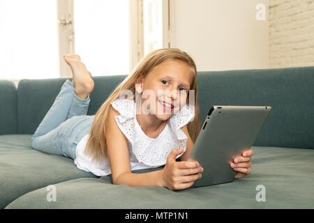 Belle blonde cute little girl playing et surf sur internet avec tablet couchée sur le canapé à la maison. L'éducation, l'utilisation d'internet, di Banque D'Images