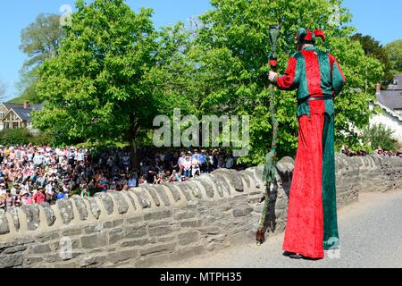 Homme debout sur échasses Clyn pont médiéval en pierre parler à crouds sur une chaude journée d'Oisans mai Green Man Festival Shropshire England UK Banque D'Images