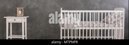 Veste enfant blanc suspendu à un lit bébé et une petite table, le ciment wall design, panorama Banque D'Images