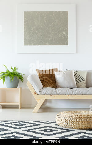 Dans un intérieur naturel blanc studio avec canapé beige, bois, plantes, pouf en rotin, graphismes et tapis à motifs Banque D'Images