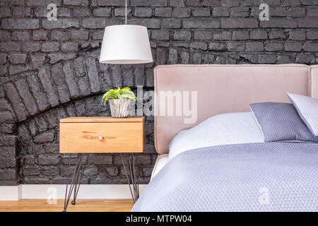 Petite plante en pot sur la table de chevet en bois sous lampe blanche dans la chambre avec mur de brique Banque D'Images