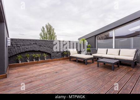 Beige et mobilier de jardin sur terrasse avec plancher en bois et mur de brique noire Banque D'Images