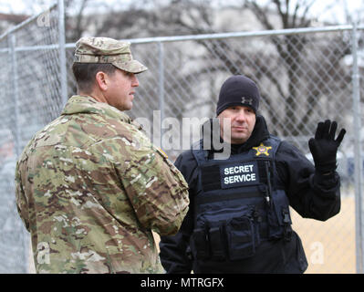 Un gardien national affecté à la foule de la Force opérationnelle communique avec un membre de la Division en uniforme des services secrets au sujet des opérations de contrôle des foules au National Mall à Washington, DC, après la cérémonie d'inauguration présidentielle le 20 janvier 2017. Le soldat, qui faisait partie de la garde nationale de l'armée de Floride, coordonnait les mesures de sécurité, surveillait les zones publiques et soutenait la dispersion ordonnée des participants. Cette opération a été menée en collaboration avec d'autres unités de la Garde nationale et des organismes fédéraux de sécurité pour assurer la sécurité et maintenir l'ordre public. Banque D'Images
