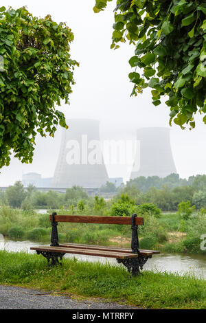 Centrale nucléaire de Belleville sur les bords de la Loire par temps brumeux avec un banc en bois sur le quai dans l'avant-plan. Banque D'Images