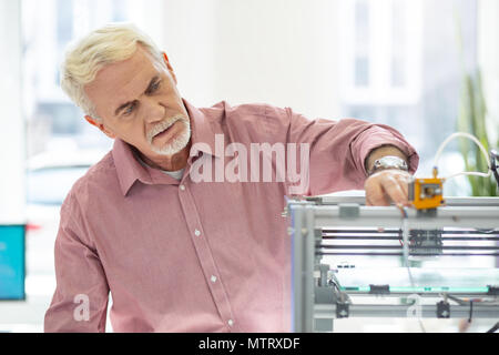 Vieil homme agréable en utilisant l'imprimante 3D au bureau Banque D'Images