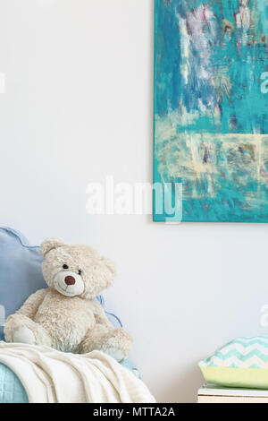 Fragment d'une peinture abstraite avec la lumière sur le mur et un ours en peluche beige sur un lit bleu Banque D'Images
