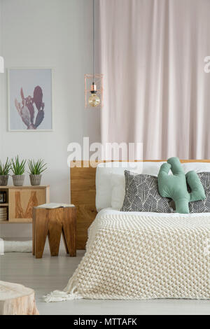 Coussin en forme de cactus vert placé sur le lit dans la chambre avec des plantes en pot et rideau rose Banque D'Images