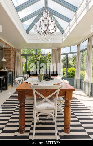 Nouveau style de salle à manger avec table en bois massif, chaise blanche, lustre et toit en verre décoratif Banque D'Images