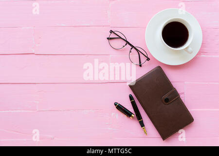 Vue de dessus de table de bureau avec espace de travail et des accessoires de bureau y compris les lunettes, stylo noir, portable et café tasse rose sur fond de bois. Banque D'Images