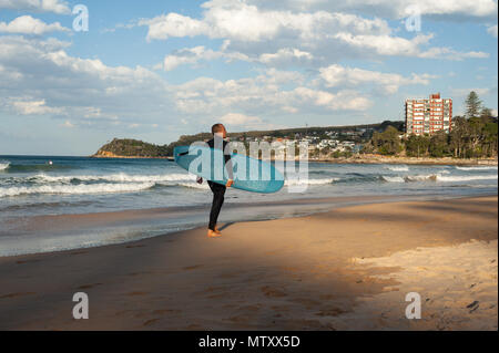 10.05.2018, Sydney, Nouvelle-Galles du Sud, Australie - un homme marche le long de la plage de Manly avec sa planche de surf sous le bras. Banque D'Images