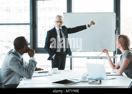 Professional senior businessman pointing at whiteboard et en regardant mes collègues au cours de réunion d'affaires Banque D'Images
