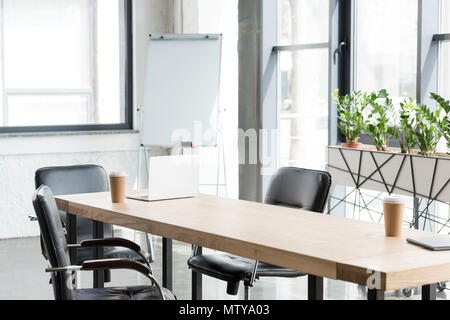 Tasses à café jetables et ordinateur portable sur une table en bois in modern office Banque D'Images