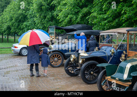 Une femme et enfant s'abriter de la pluie sous un parapluie colorés comme ils regardent une sélection de rare et élégant et classique avant 1918 voitures anciennes lors d'un événement à Midhurst, West Sussex, UK. Banque D'Images