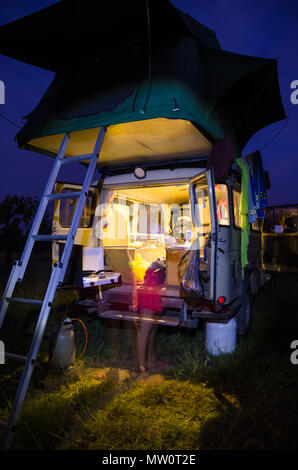 L'extrémité arrière du véhicule de camping 4x4 avec tente sur le toit et motion blurred woman cooking allumé pendant la nuit. Banque D'Images