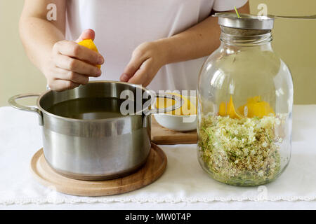 Des fleurs, de l'eau, de citron et de sucre, les ingrédients et une femme en train de préparer un sirop de sureau. De style rustique, selective focus. Banque D'Images