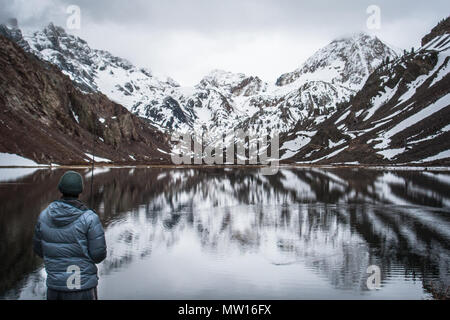 Un homme pêche dans un lac avec de grandes montagnes couvertes de neige dans l'arrière-plan. Banque D'Images