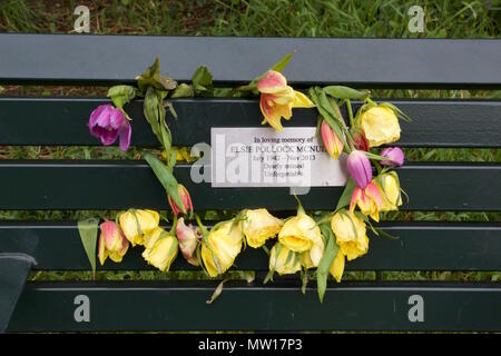 Un mémorial banc avec une plaque métallique entouré de fleurs en train de mourir à l'intérieur de Tower Hamlets Cemetery Park Banque D'Images