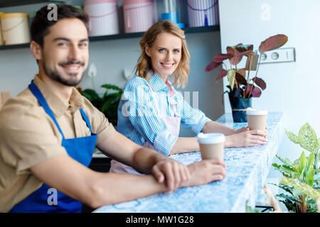 Deux jeunes travailleurs dans les tabliers de boire du café and smiling at camera Banque D'Images