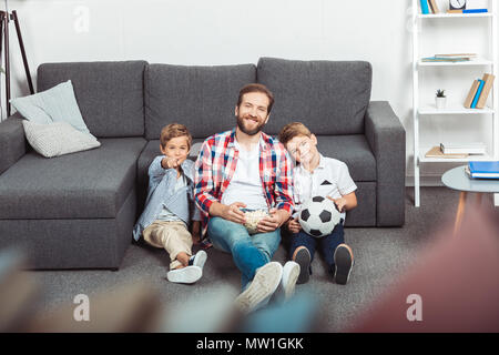 Avec père fils eating popcorn tout en regardant un match de football à la maison Banque D'Images