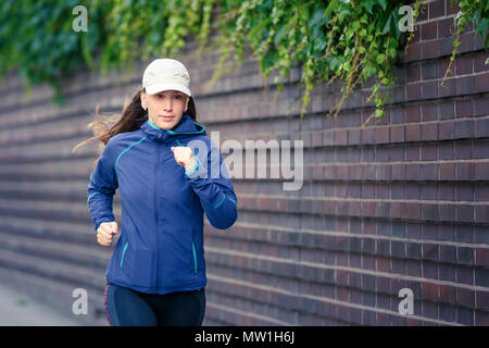 Young woman jogging le long de la rue en ville européen, dans la matinée. L'exécution de fitness petite fille contre le mur de briques. Image tonique Banque D'Images