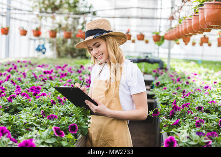 Jeune femme propriétaire de serre dans le presse-papiers afin de remplissage de fleurs Banque D'Images