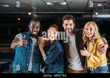Jeunes amis multiethnique montrant Thumbs up at bowling club Banque D'Images
