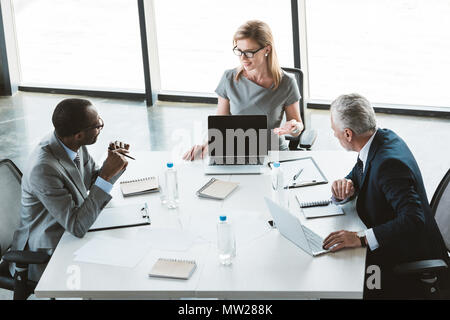 Portrait of businesswoman showing ordinateur portable avec écran blanc et à la réunion de collègues masculins au cours de Banque D'Images