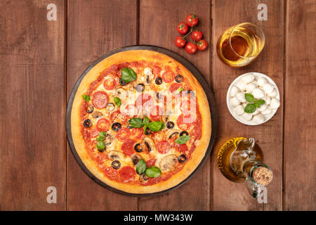 Photo prise à la verticale de la pizza au pepperoni, avec verre de vin blanc, huile d'olive, tomates cerises et mozzarellini fromage, tourné à partir de ci-dessus sur dark background rustique Banque D'Images