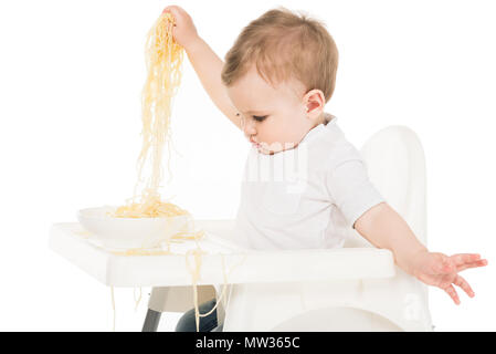 Baby Boy holding spaghetti dans les mains et assis dans une chaise haute isolé sur fond blanc Banque D'Images