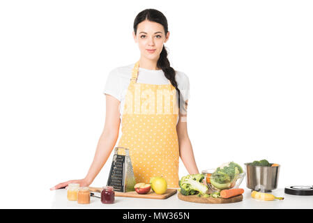 Femme en tablier, debout à table avec des fruits, des légumes, les planches à découper, une râpe, pots avec purée et casserole Banque D'Images