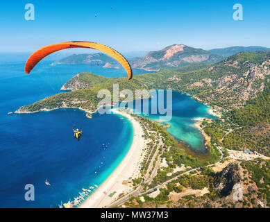 Parachute dans le ciel. Tandem parapente voler au-dessus de la mer avec de l'eau bleue et les montagnes en journée ensoleillée. Vue aérienne de la bleue et de parapente Banque D'Images