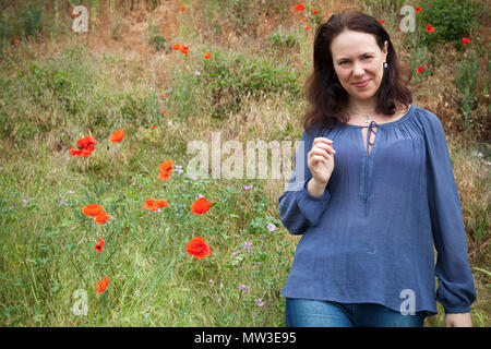 Souriante jeune femme européenne adultes marche sur une prairie d'été avec la floraison des coquelicots. Portrait en extérieur Banque D'Images