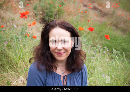 Outdoor portrait of smiling young woman européenne repose sur une prairie d'été avec la floraison des coquelicots Banque D'Images