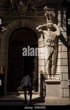 Les Atlantes sous la figure du sculpteur H.A. Pegram (1896) à l'entrée de Drapers' Hall livery company à Throgmorton Street, un portier Stoops to pick up a chuté clés en dehors de tabliers en Throgmorton Street, dans la ville de Londres, le quartier financier de la capitale, alias le Square Mile, le 15 mai 2018, à Londres, au Royaume-Uni. Les tabliers' Company est une société livrée dans la ville de Londres dont les racines remontent au 13ème siècle, lorsque comme son nom l'indique, il a été impliqué dans le commerce de draperie. Bien qu'il n'est plus impliquée dans le commerce, l'entreprise a évolué l'acquisition d'une nouvelle pertinence. Il Banque D'Images